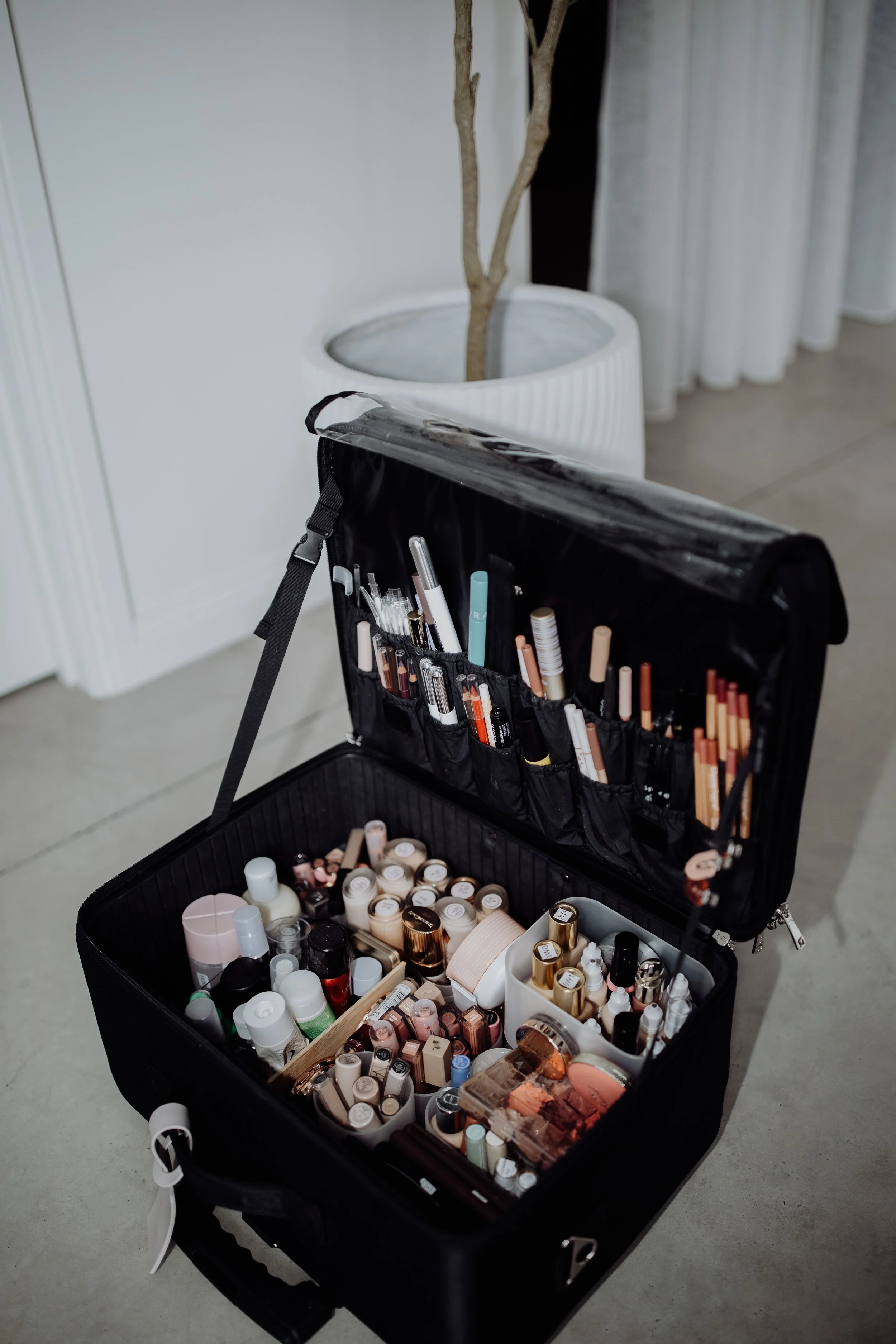Open black makeup case filled with skincare and makeup products, with organized brushes and tools inside.