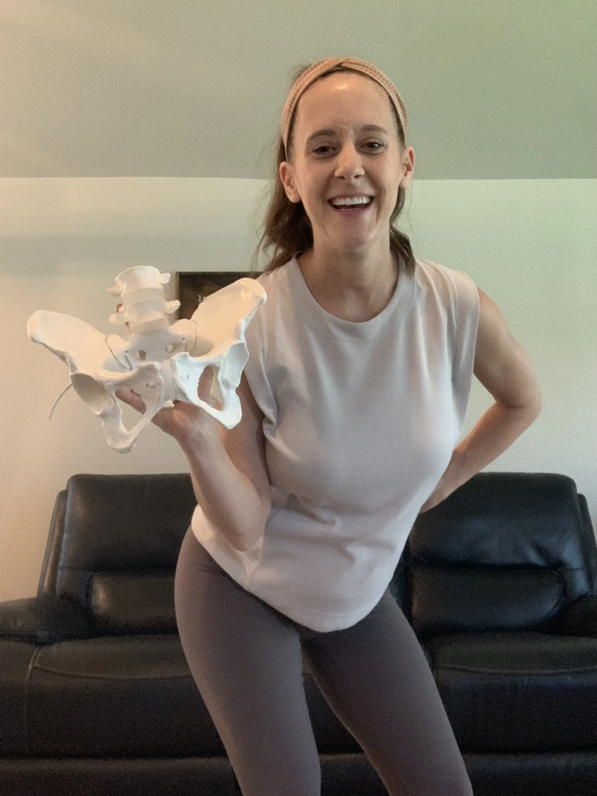 Woman smiling and holding a model of a human lower spine and pelvis in a living room