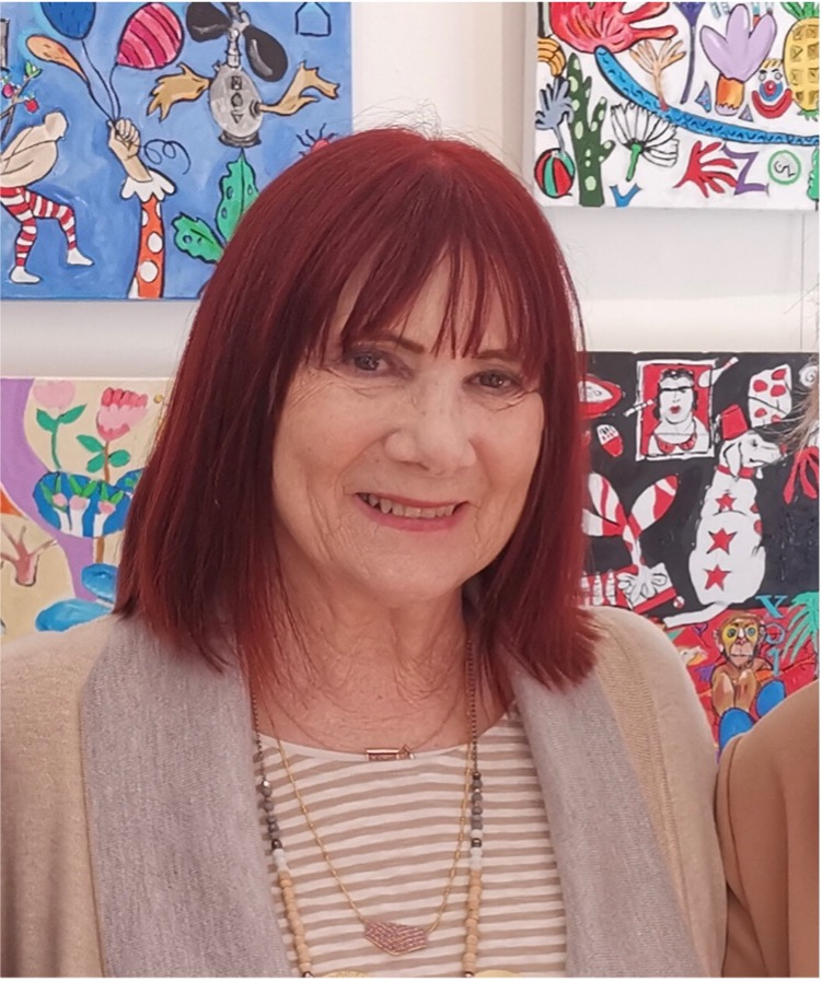 A woman with shoulder-length red hair smiling in front of colorful abstract artwork.