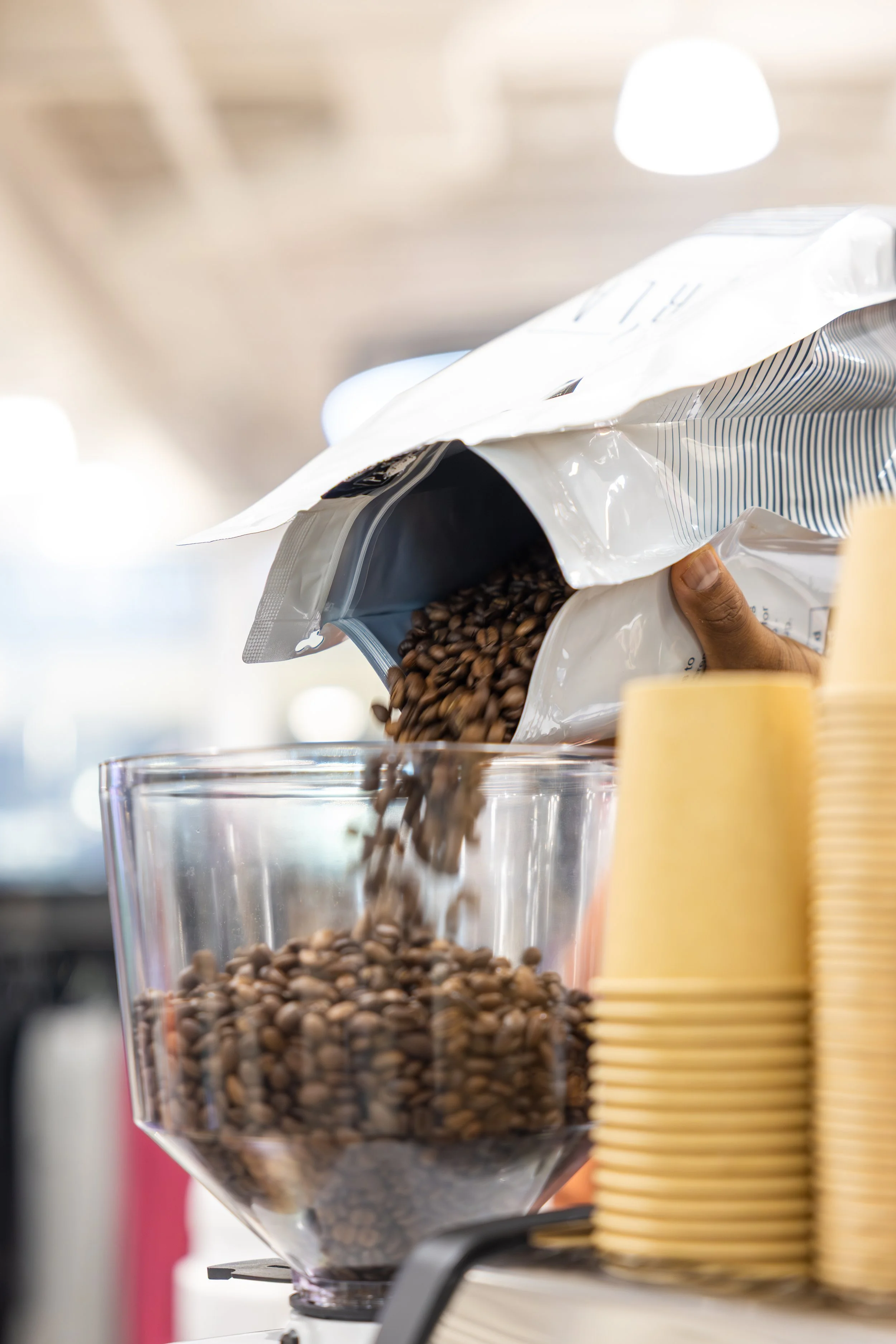Pouring coffee beans from a bag into a glass container at a coffee shop or store.