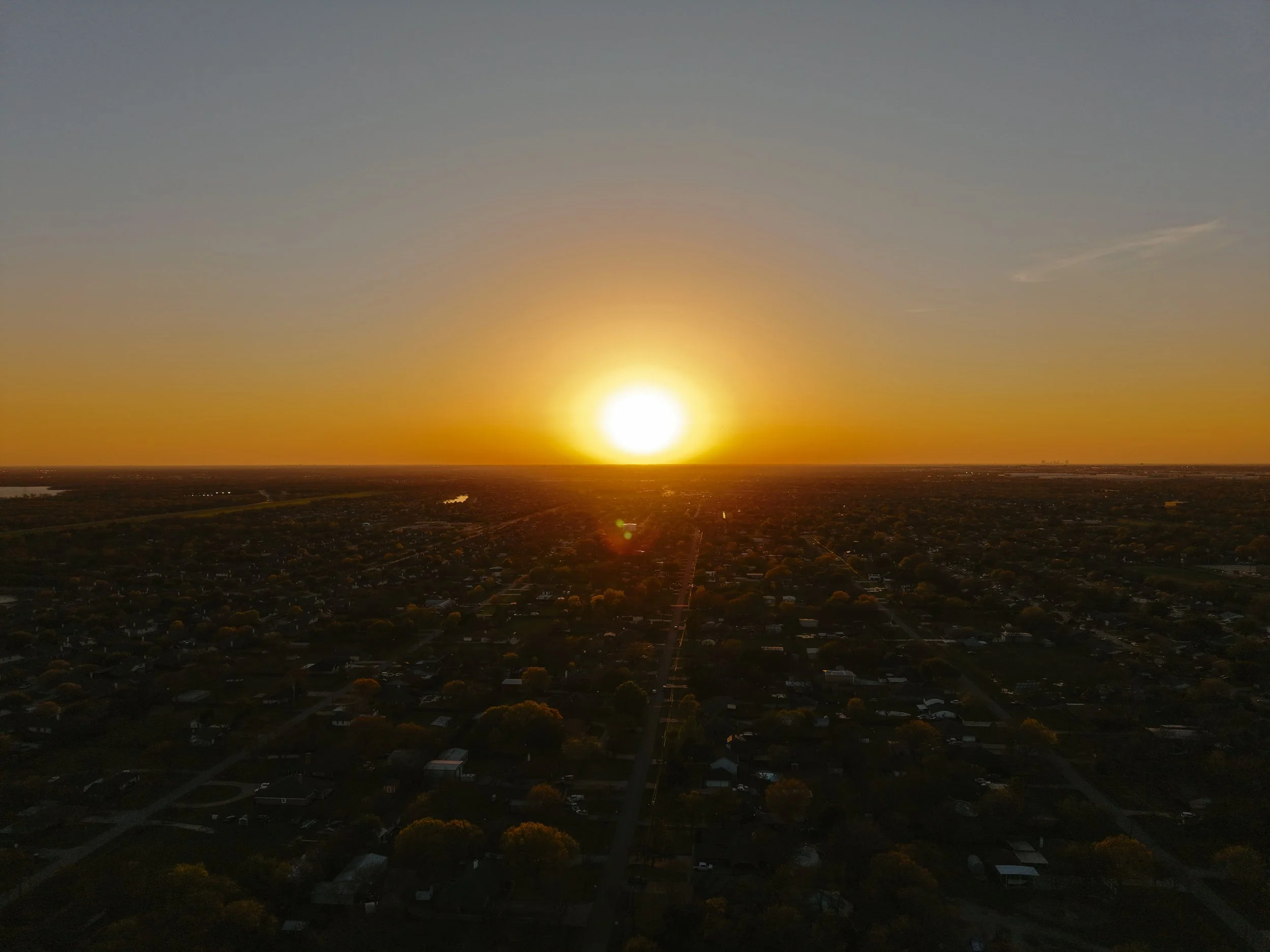 Aerial view of a city during sunset, with the sun low on the horizon and the sky gradually darkening.