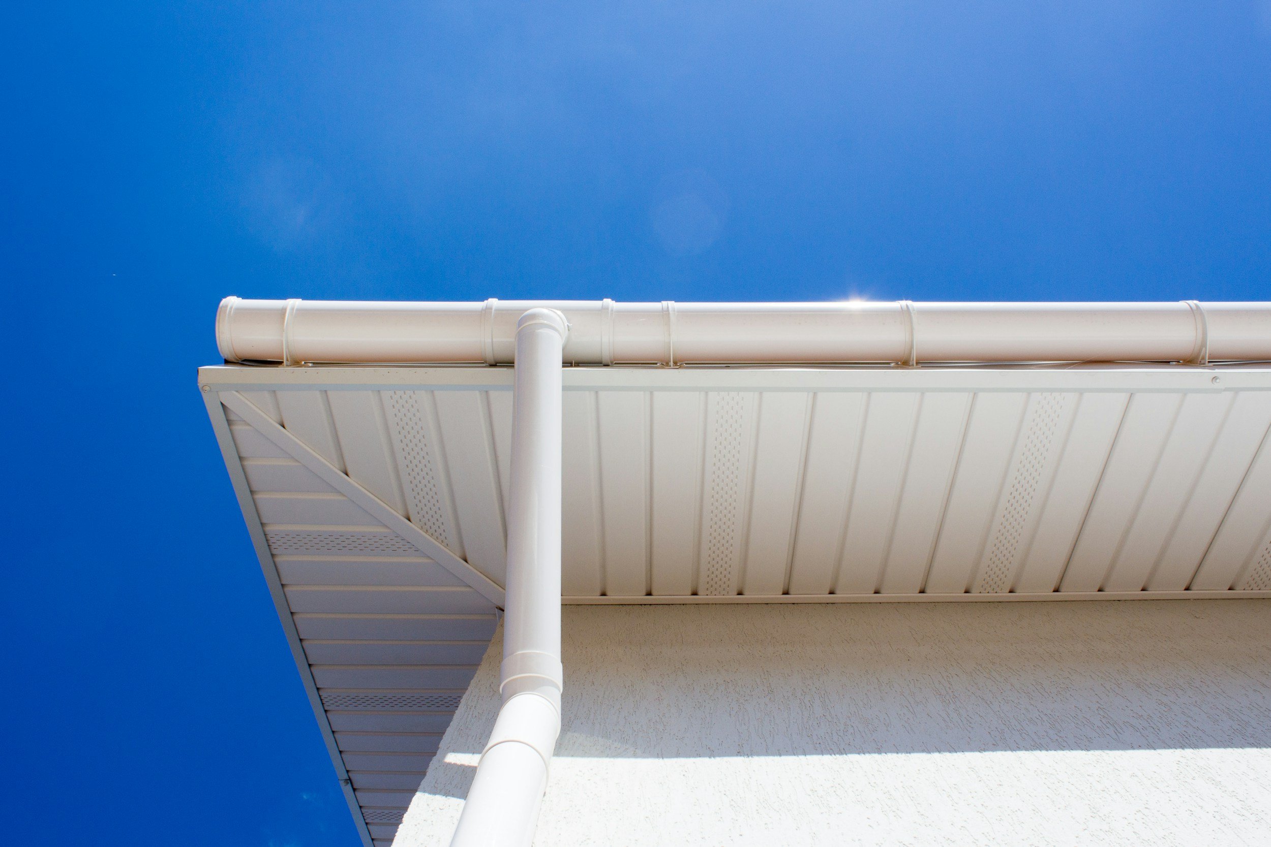 Close-up view of a white building's roof with gutters and downspout against a clear blue sky.