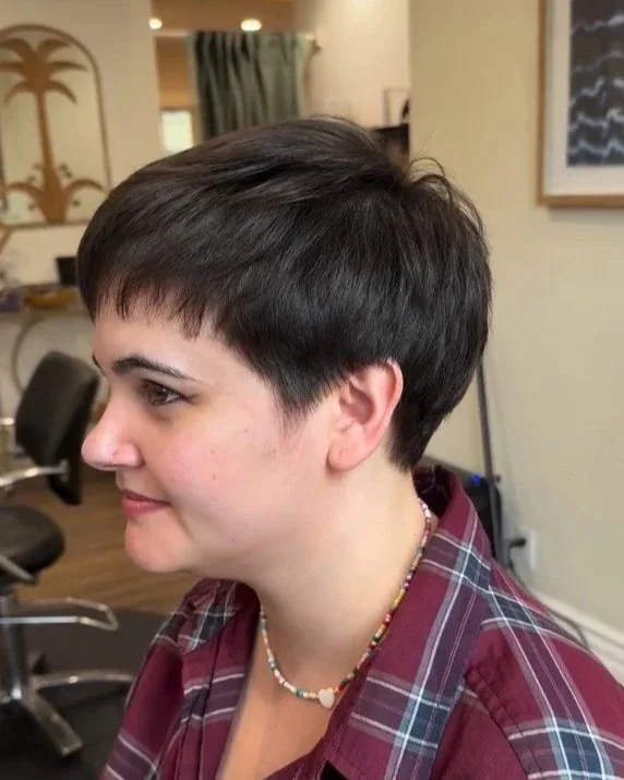 A woman with short, dark hair and a plaid shirt sitting in a hair salon. Hairstyle done by Caitlin Duffy Hairstylist at Bolt Collective Hair Salon in Pleasanton, CA.