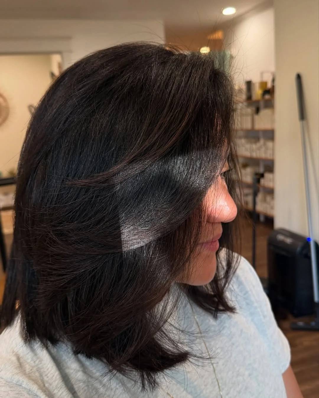 A woman with shoulder-length dark brown hair styled with layers and soft waves, sitting indoors. Hairstyle done by Caitlin Duffy Hairstylist at Bolt Collective Hair Salon in Pleasanton, CA.