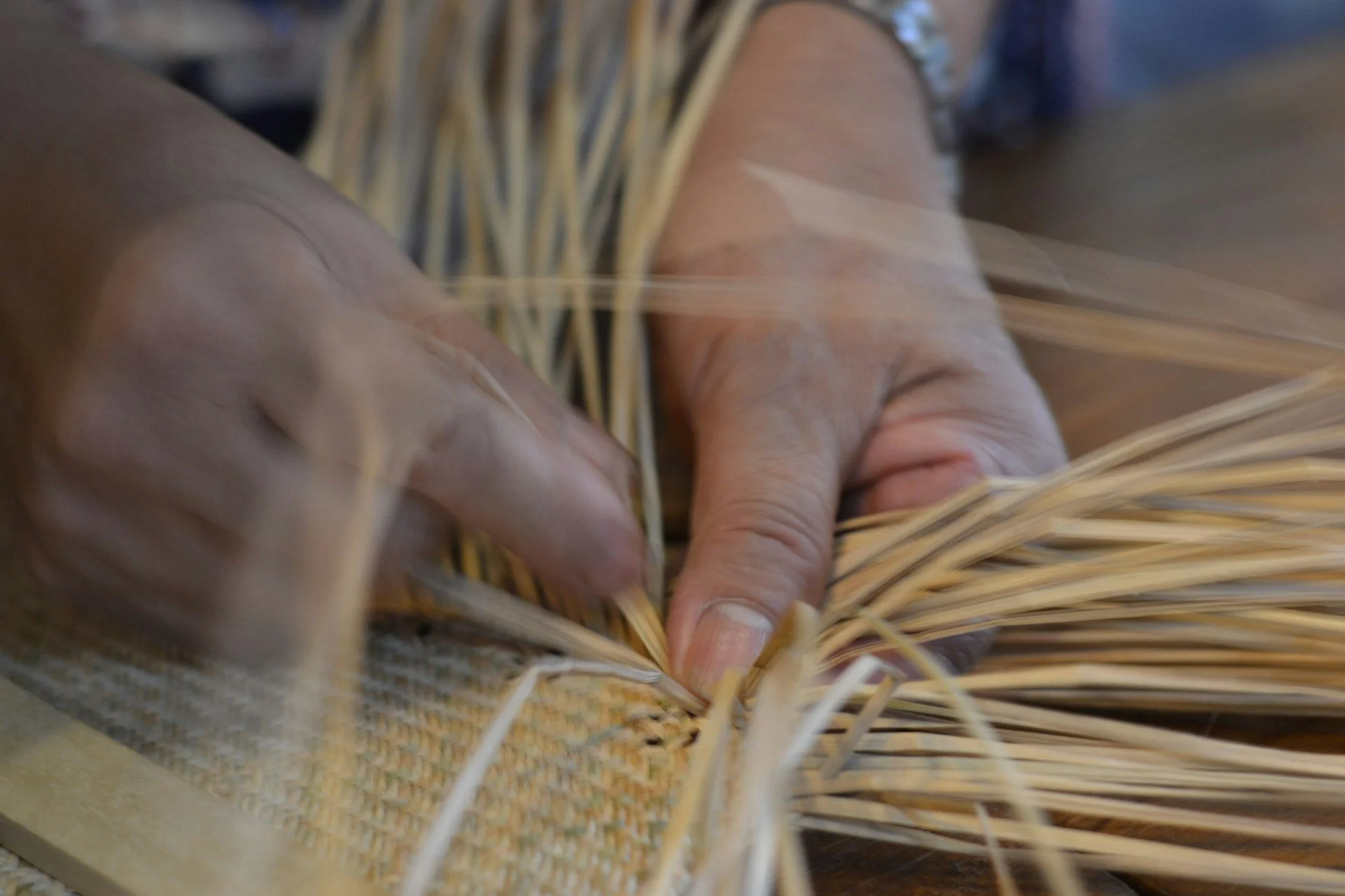 Close-up of hands weaving a basket from natural reeds or straw.