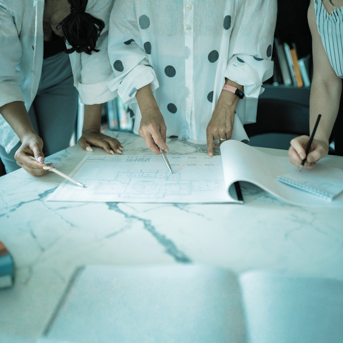 People reviewing and discussing architectural plans on a table with blueprints and drawing tools.