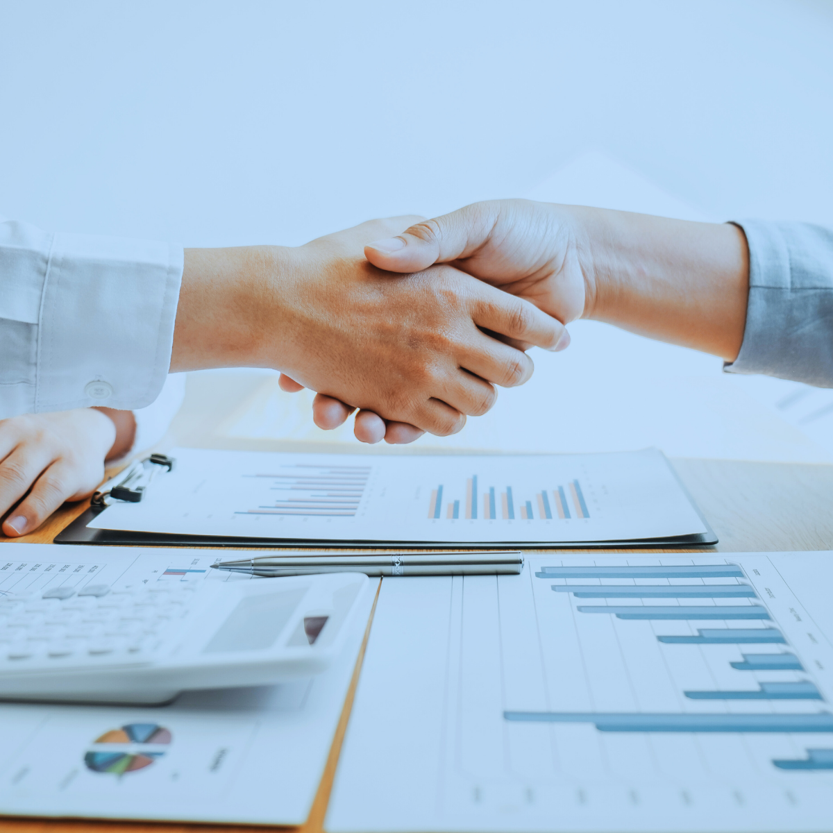 Two people shaking hands over a desk with financial documents and a calculator.
