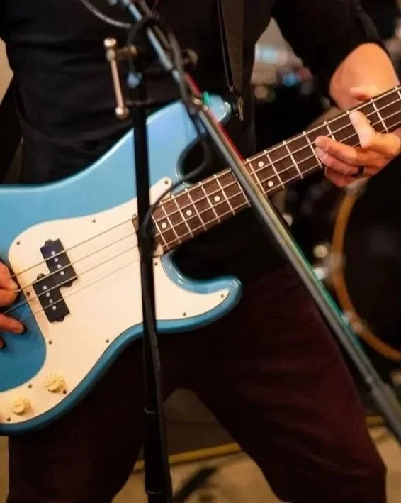 A person playing a blue electric bass guitar in a music setting, with a microphone stand in front.