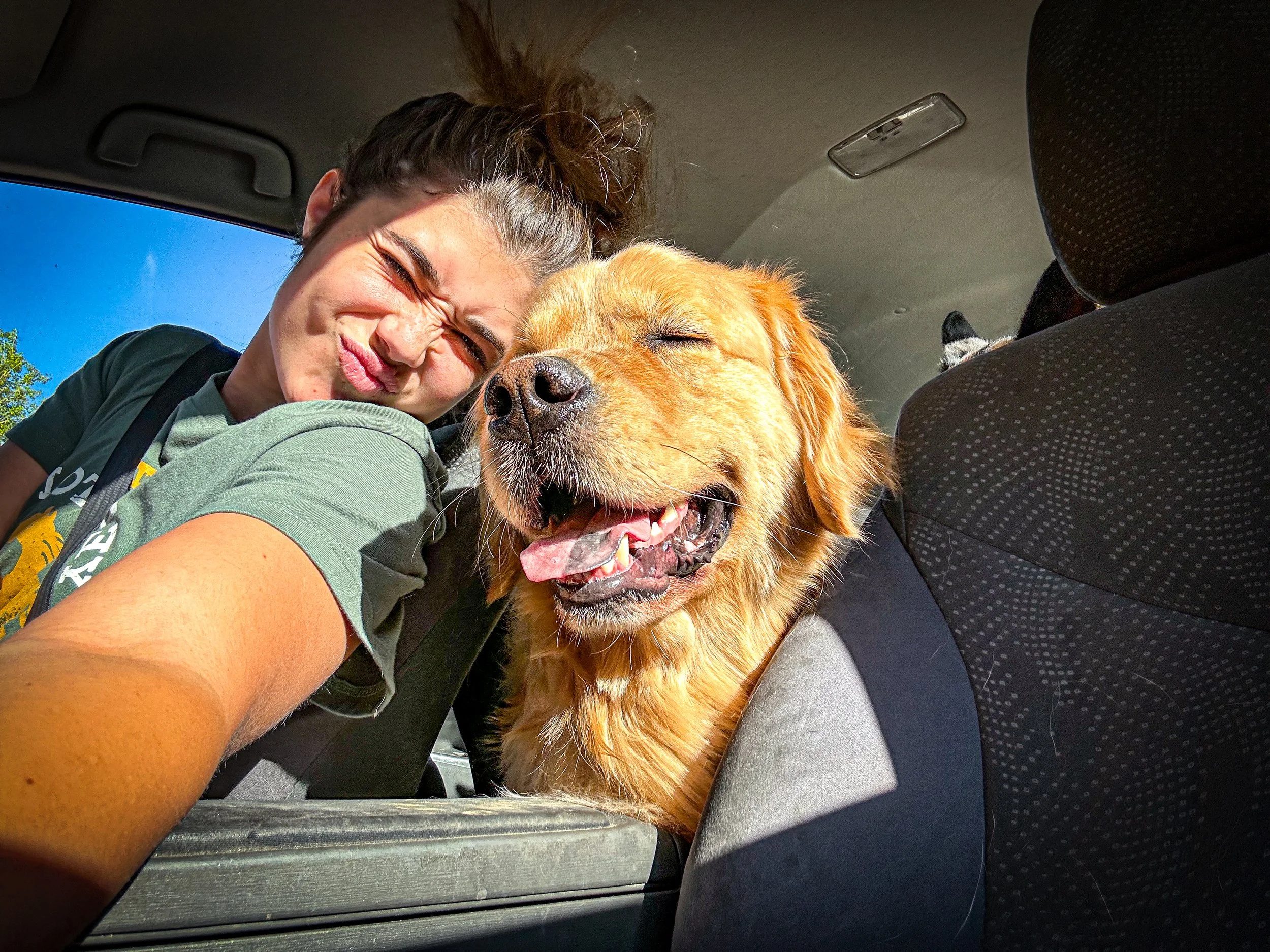 Woman and golden retriever dog smiling and cuddling in a car, with a clear blue sky outside -Dog Overnight Boarding in La Quinta CA