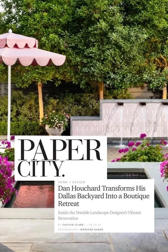 A backyard patio with a pink umbrella, market-style planters with pink and purple flowers, and a textured white wall with a water feature. A large cover with the text "PAPER CITY" and a headline about Dan Houchard's Dallas backyard transformation into a boutique retreat.