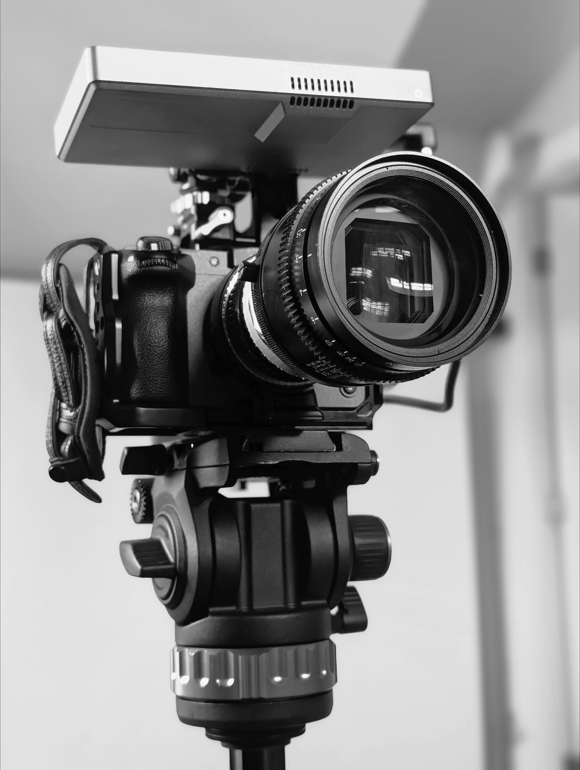 Black and silver professional camera mounted on a tripod with a large lens and mounted accessory.