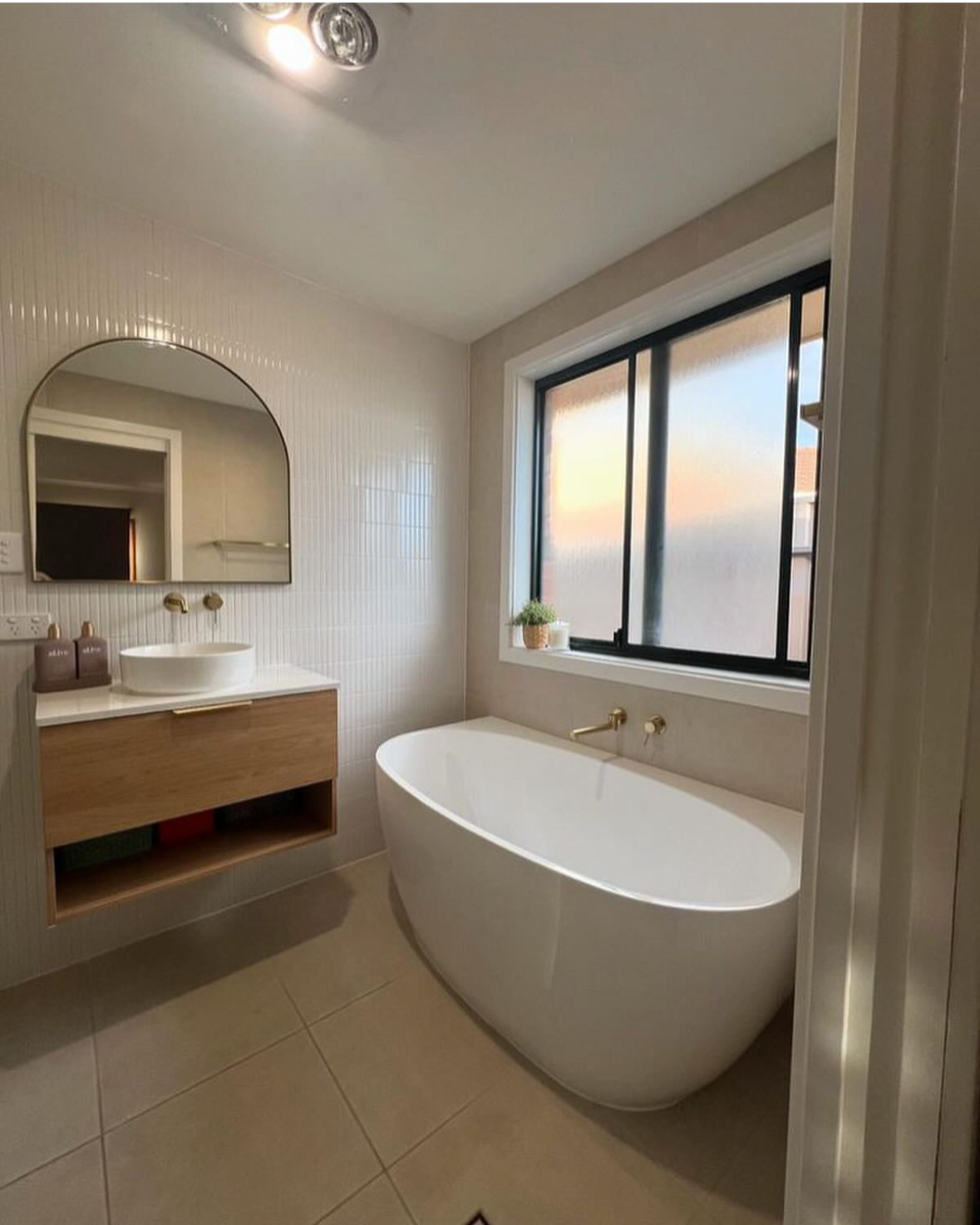 Modern bathroom with a freestanding bathtub, a large window, a wall-mounted sink, a mirror, and minimal decor.