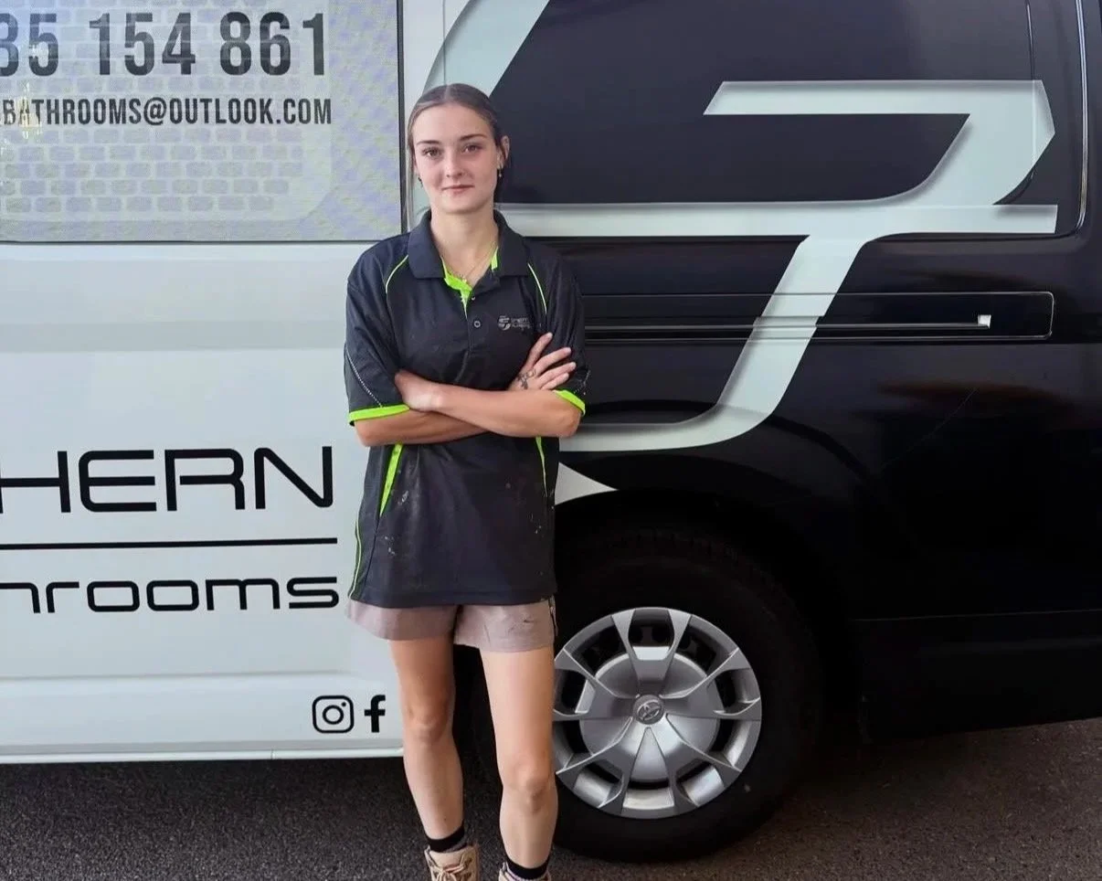 A young woman standing with arms crossed in front of a black and white van displaying business contact information and social media icons.