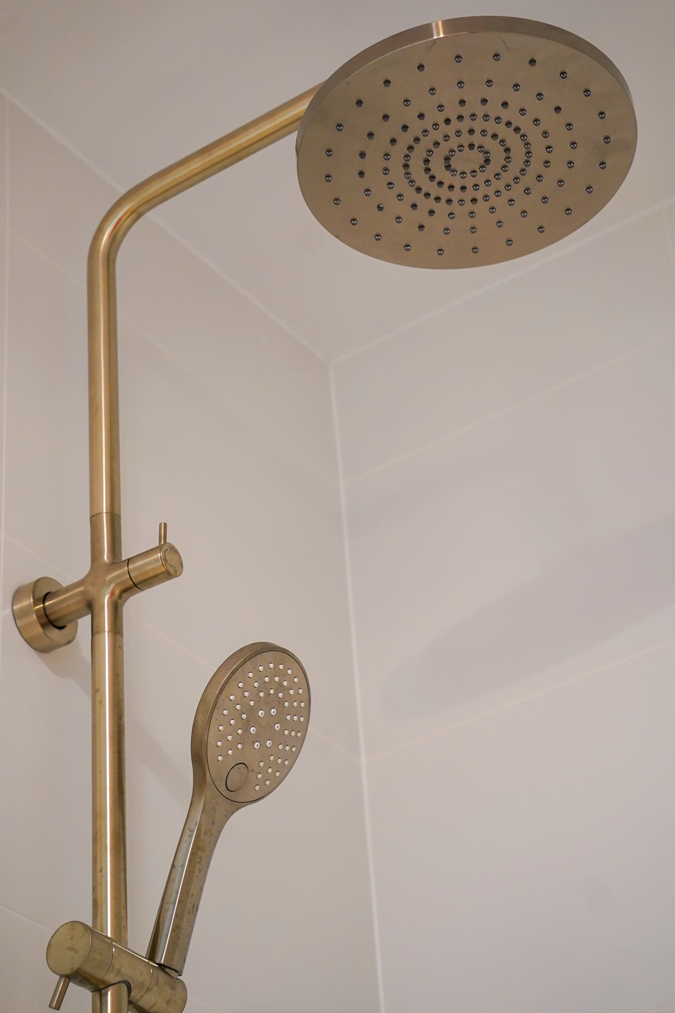 A showerhead with multiple nozzles and a handheld spray head attached to a metal pipe against a tiled wall.