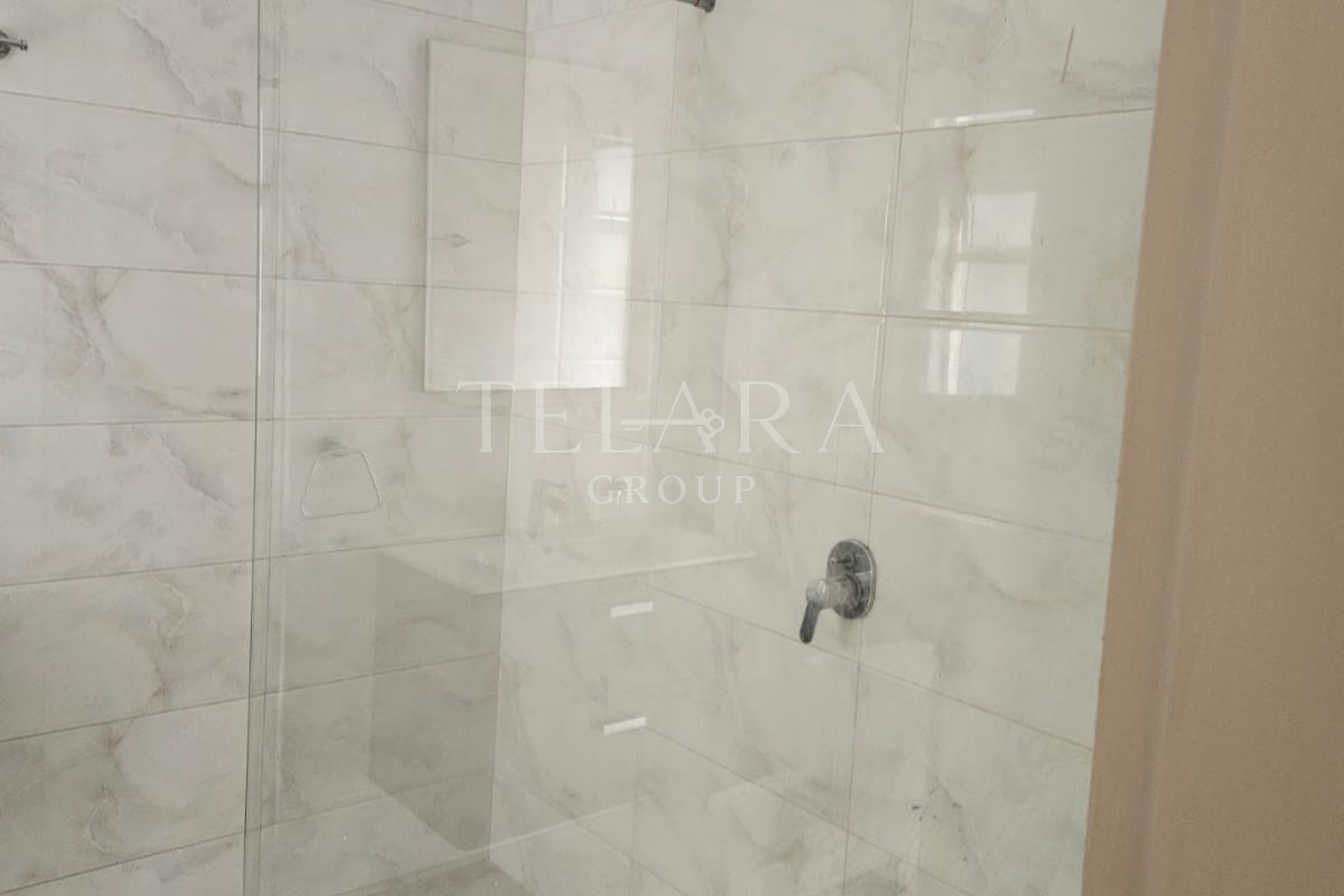 Empty shower area with white marble tiles, a glass shower door, and a single faucet handle.