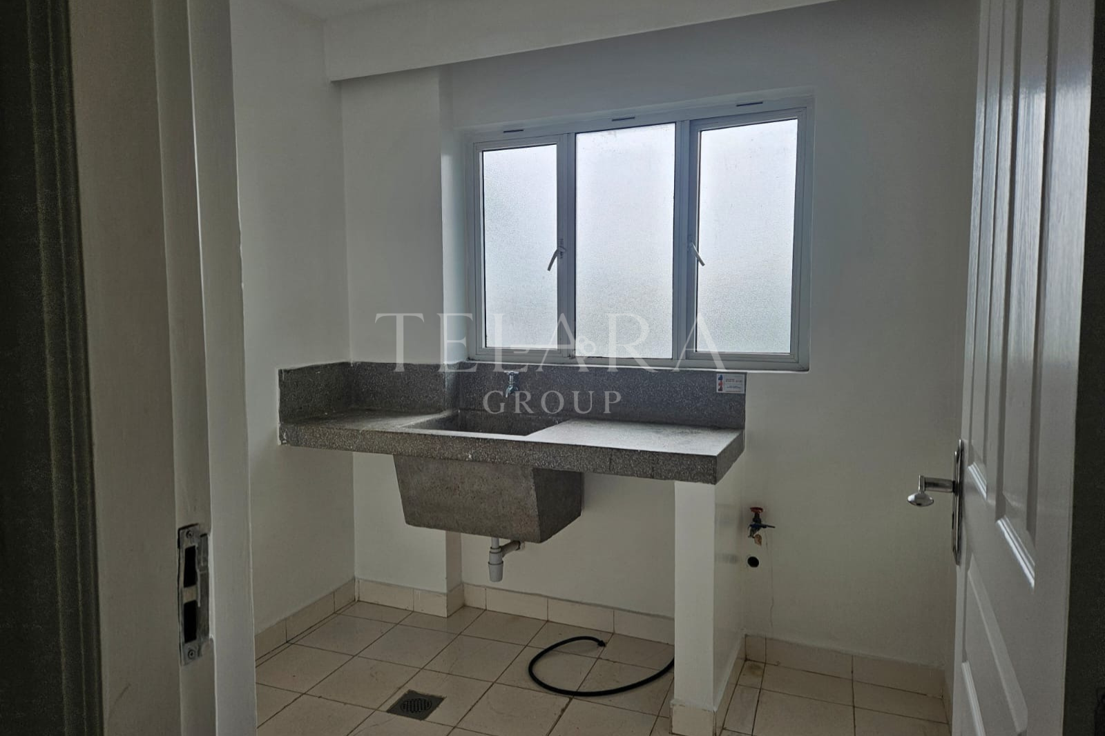 Empty laundry room with a concrete utility sink, a window, a door on the right, and no appliances or fixtures installed yet.