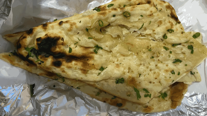 Grilled naan bread topped with melted cheese and chopped green onions.