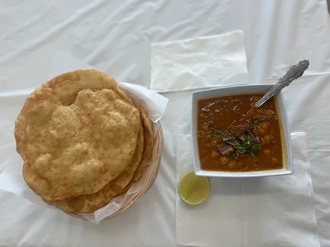 Basket of fried Indian bread with a bowl of chickpea curry and a lemon wedge on a white table.