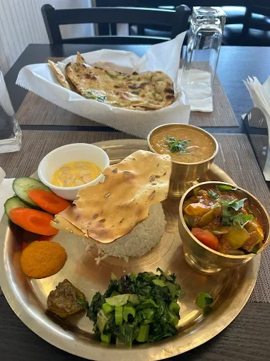 An Indian thali platter with various dishes including rice, curry, vegetables, fried item, chutney, flatbread, and salad on a metal tray, set on a wooden table.