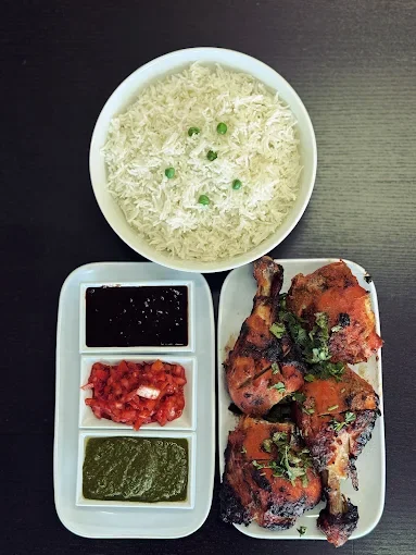 Plate with grilled chicken, bowls of salsa, green chutney, and a bowl of rice garnished with peas.