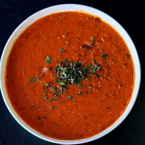 A bowl of tomato-based Indian curry garnished with chopped cilantro.
