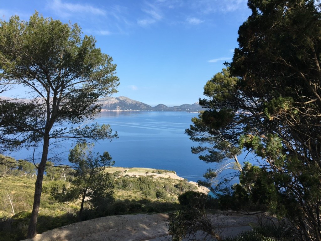 A scenic view of a large blue lake surrounded by green trees and mountains in the distance under a partly cloudy sky.