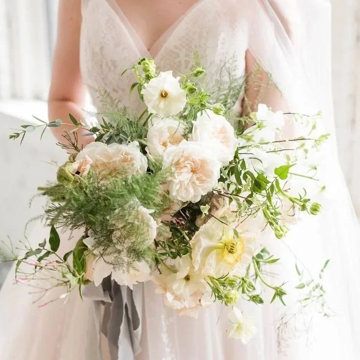 A Reno bride holding a bouquet of white and pale pink flowers with green foliage, in front of her wedding dress.
