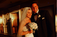 A Tahoe bride and groom smiling, standing indoors during their wedding celebration. The bride holds a bouquet of white flowers, and the groom wears a black tuxedo with a bow tie.
