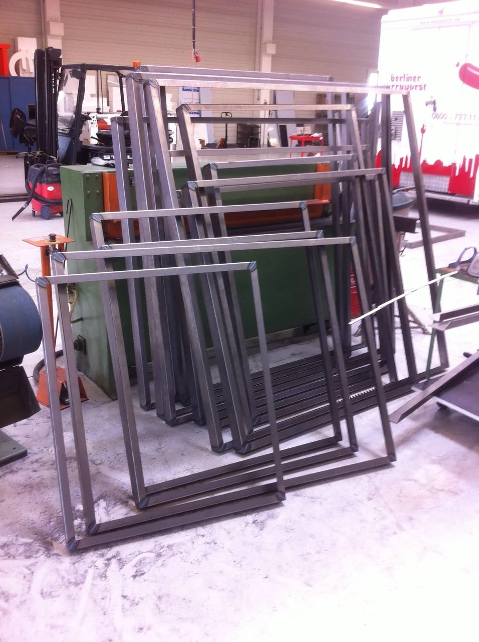 Stacked metal frames and a forklift inside a workshop.