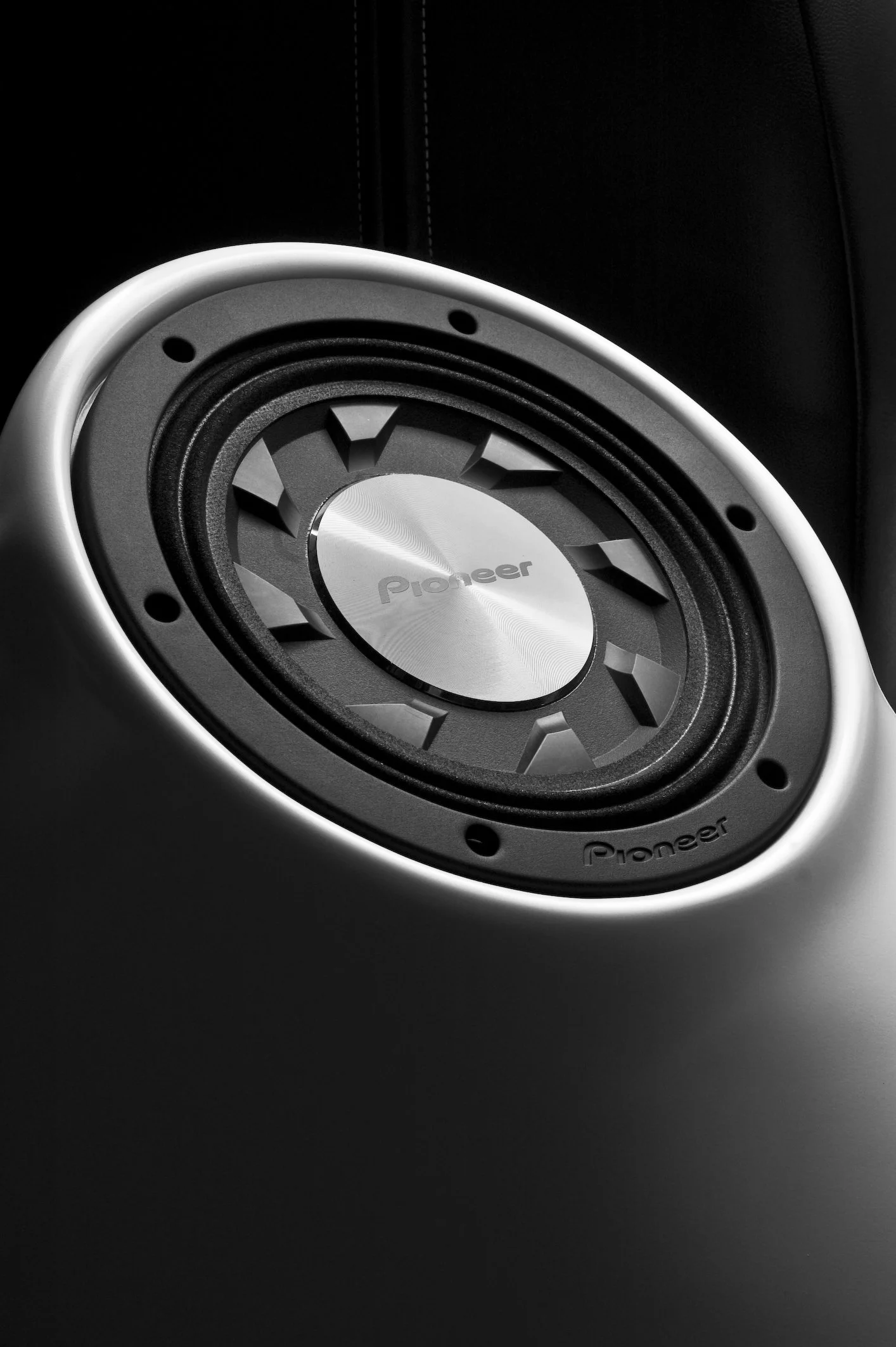 Black and white close-up of a Pioneer speaker embedded in a smooth surface.