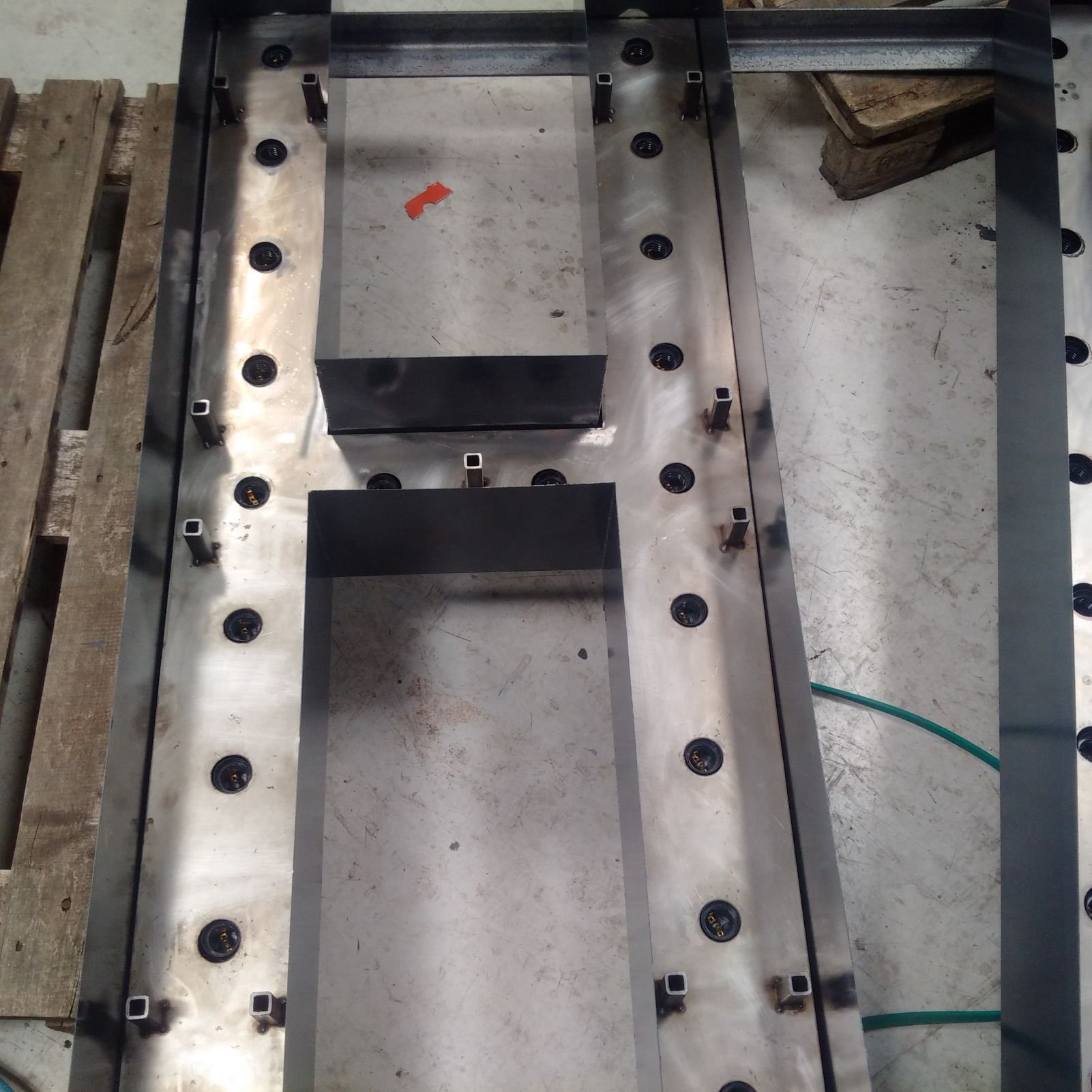 Metal table frame with evenly spaced bolt holes, some upright metal supports, and wood blocks in the background.