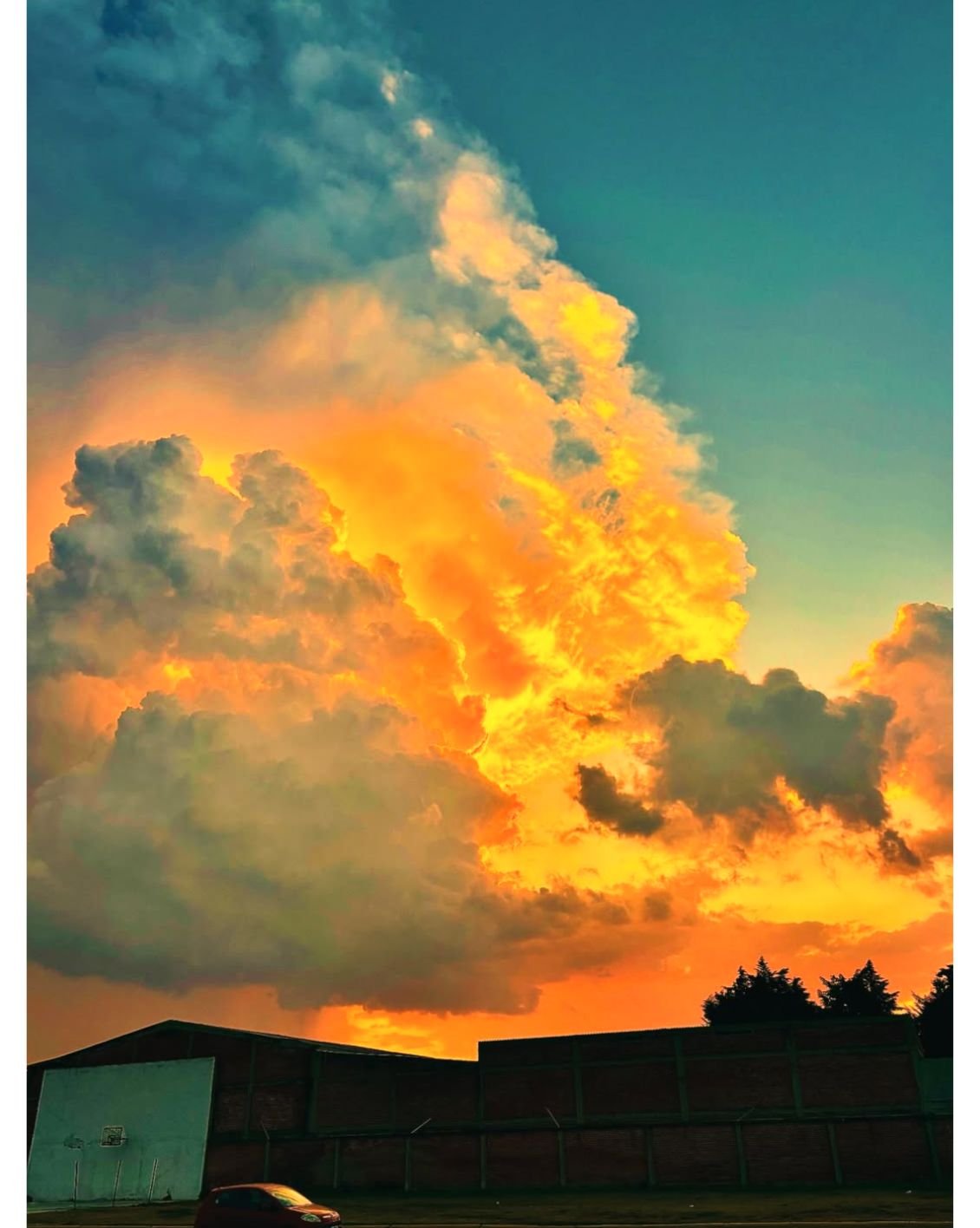 Colorful sunset sky with orange, yellow, and blue clouds over a silhouette of a building and trees.