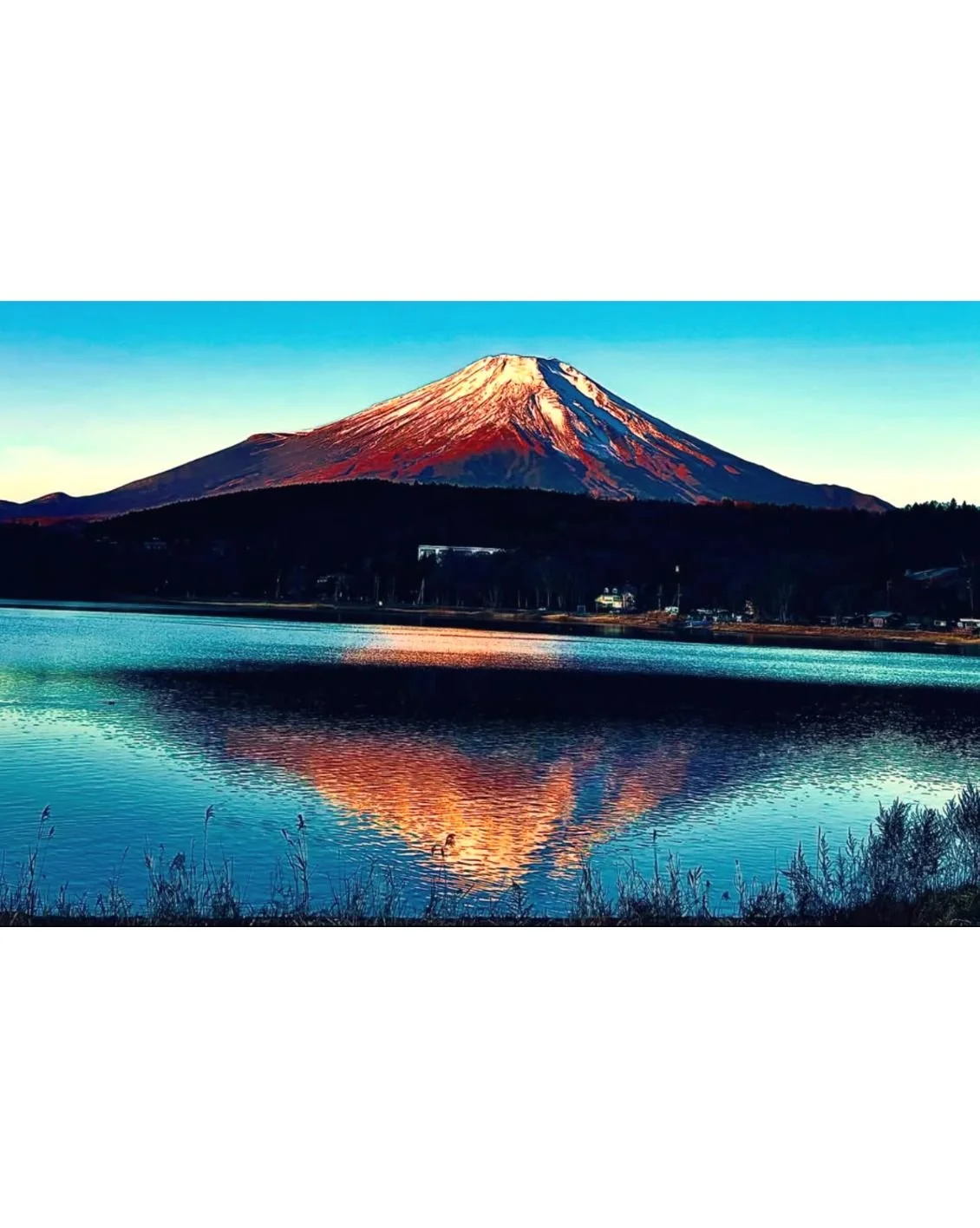 Snow-capped Mount Fuji reflected in a lake during sunset.