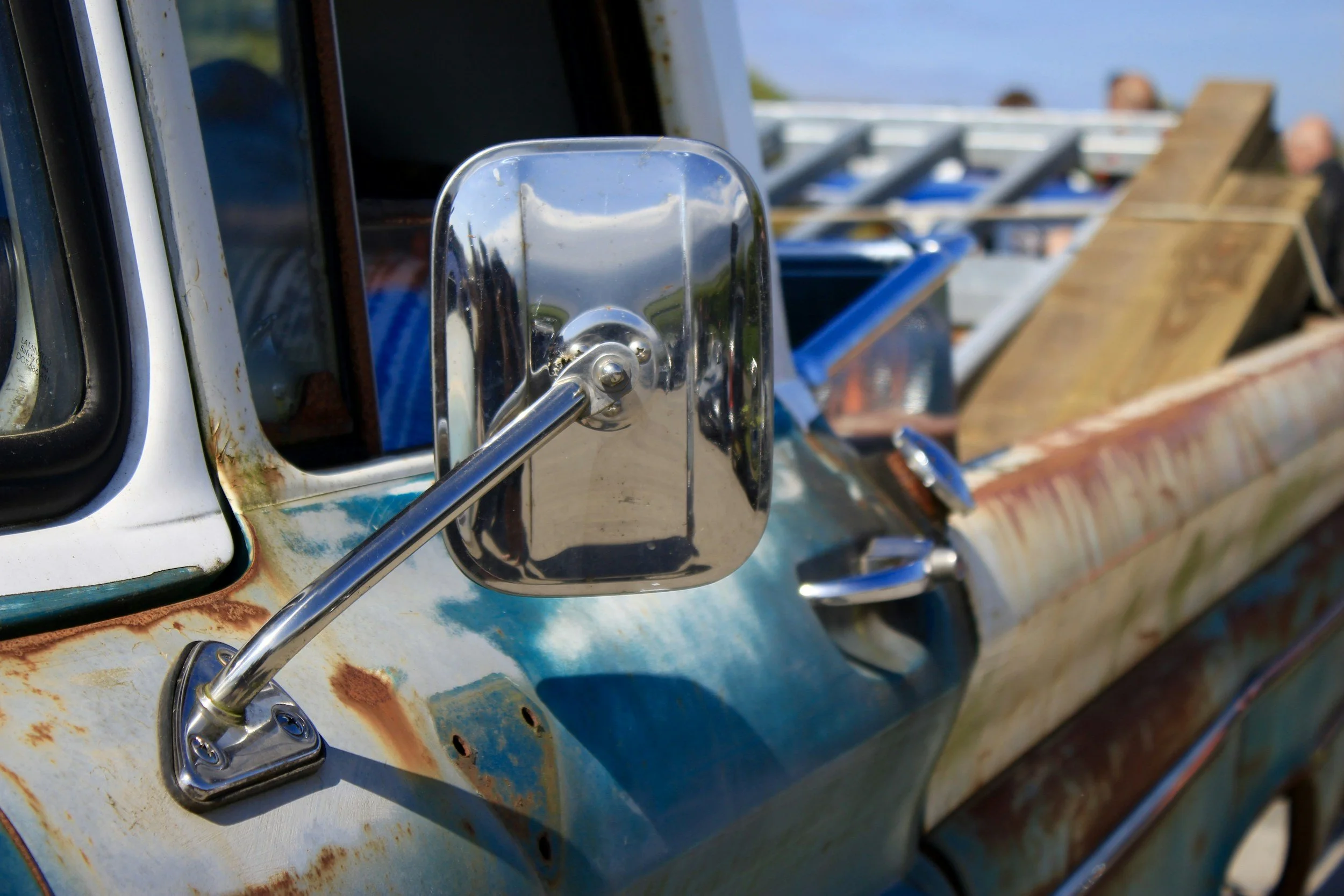 Close-up of a rusty, vintage pickup truck with a shiny side mirror and a cargo bed filled with wooden pallets and blue containers.