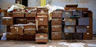 A large collection of stacked cardboard boxes and storage containers on a warehouse floor.