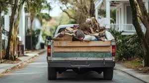 Pickup truck filled with trash and debris, driving down a residential street with trees and houses.
