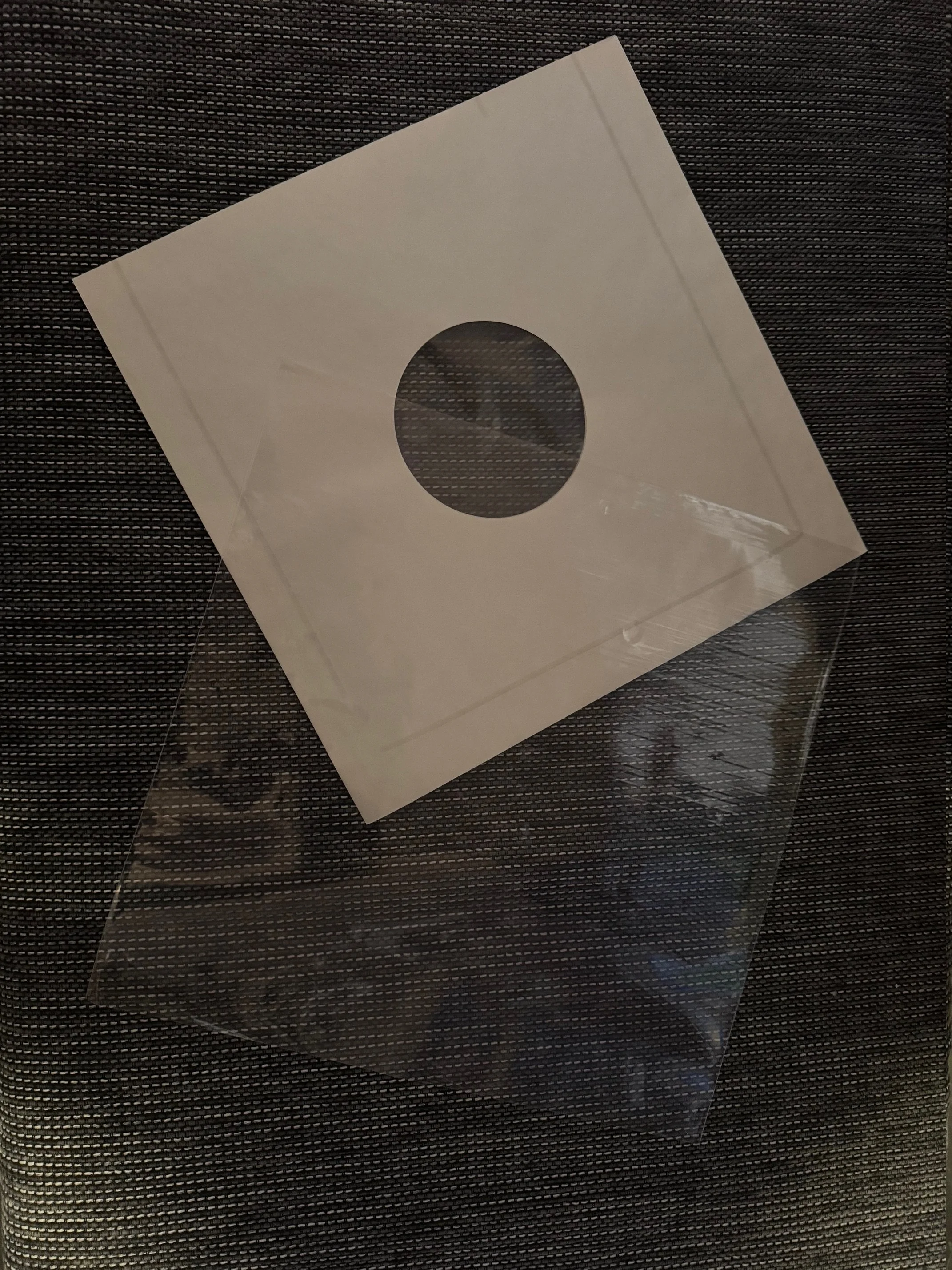 Et hvitt kvadratisk objekt med et rundt hull i midten, plassert på en mørk overflate.