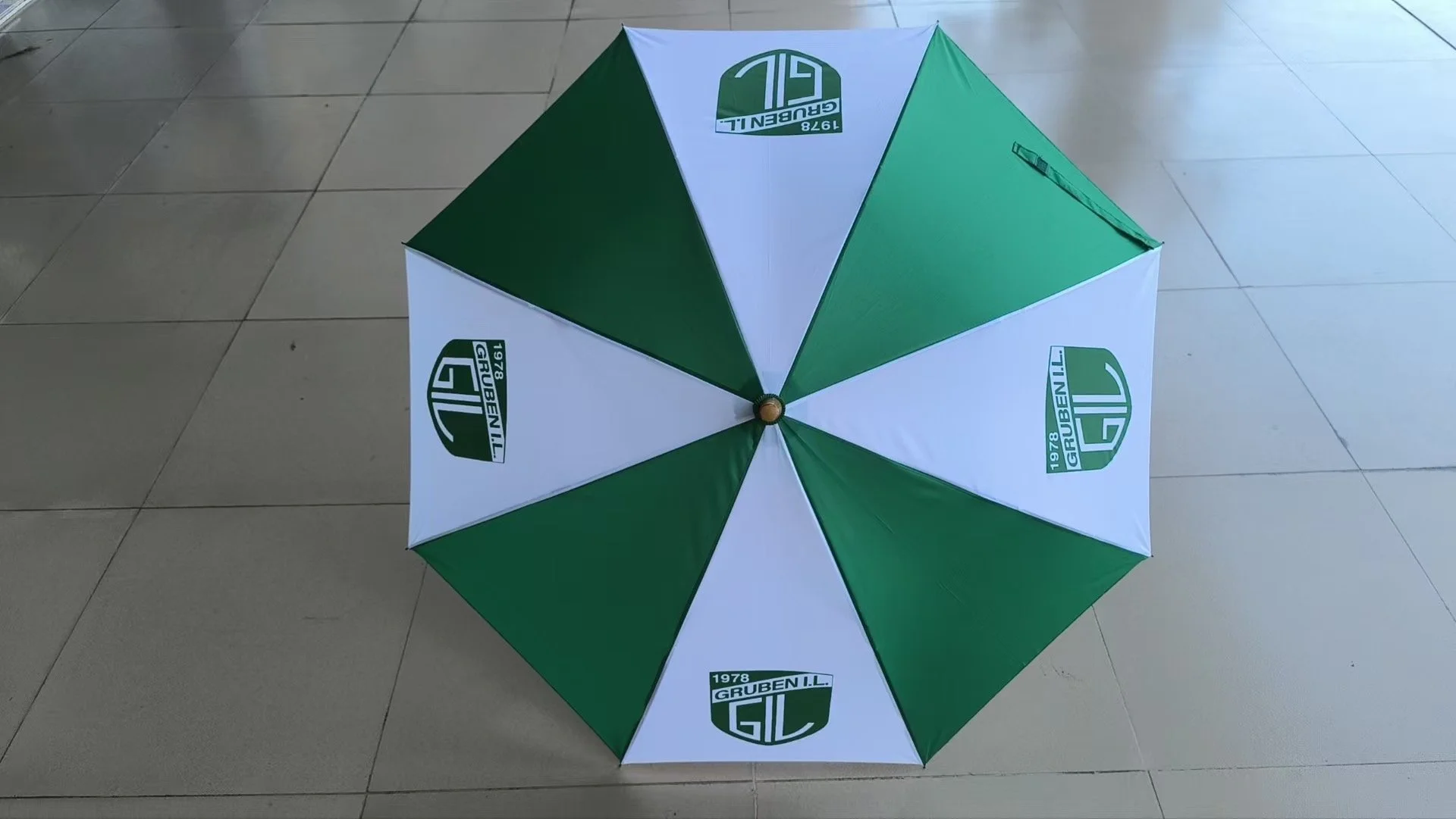 En åpen paraply med grønne og hvite paneler, som har logoen til Gruben I.L. og påskriften 1978 på hvite paneler.