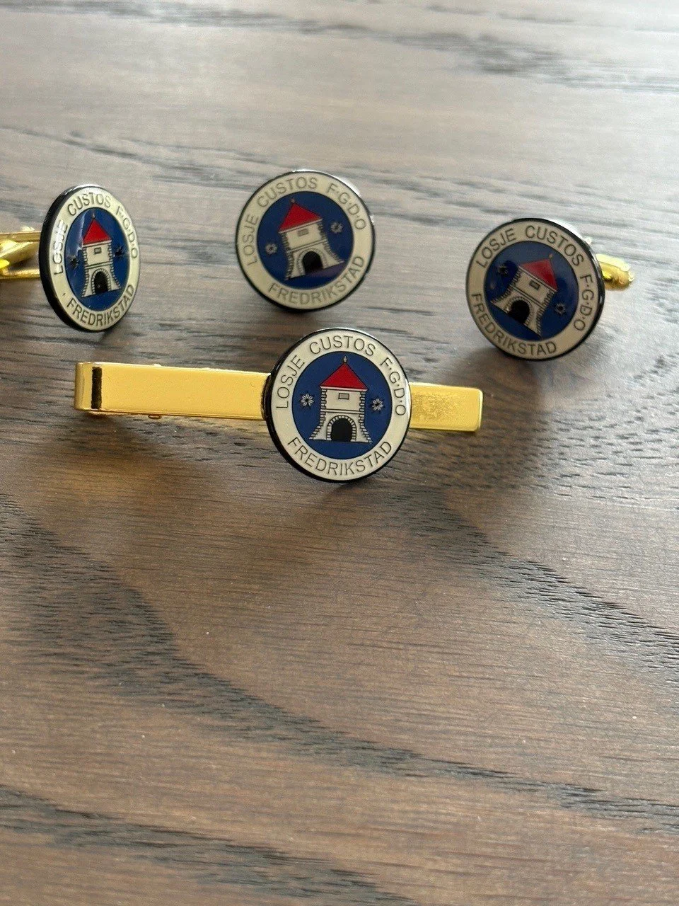 Klokker og mansjettknapper med bygningssymbol og teksten "LOSJE CUSTOS F.G.D.O. FREDRIKSTAD".