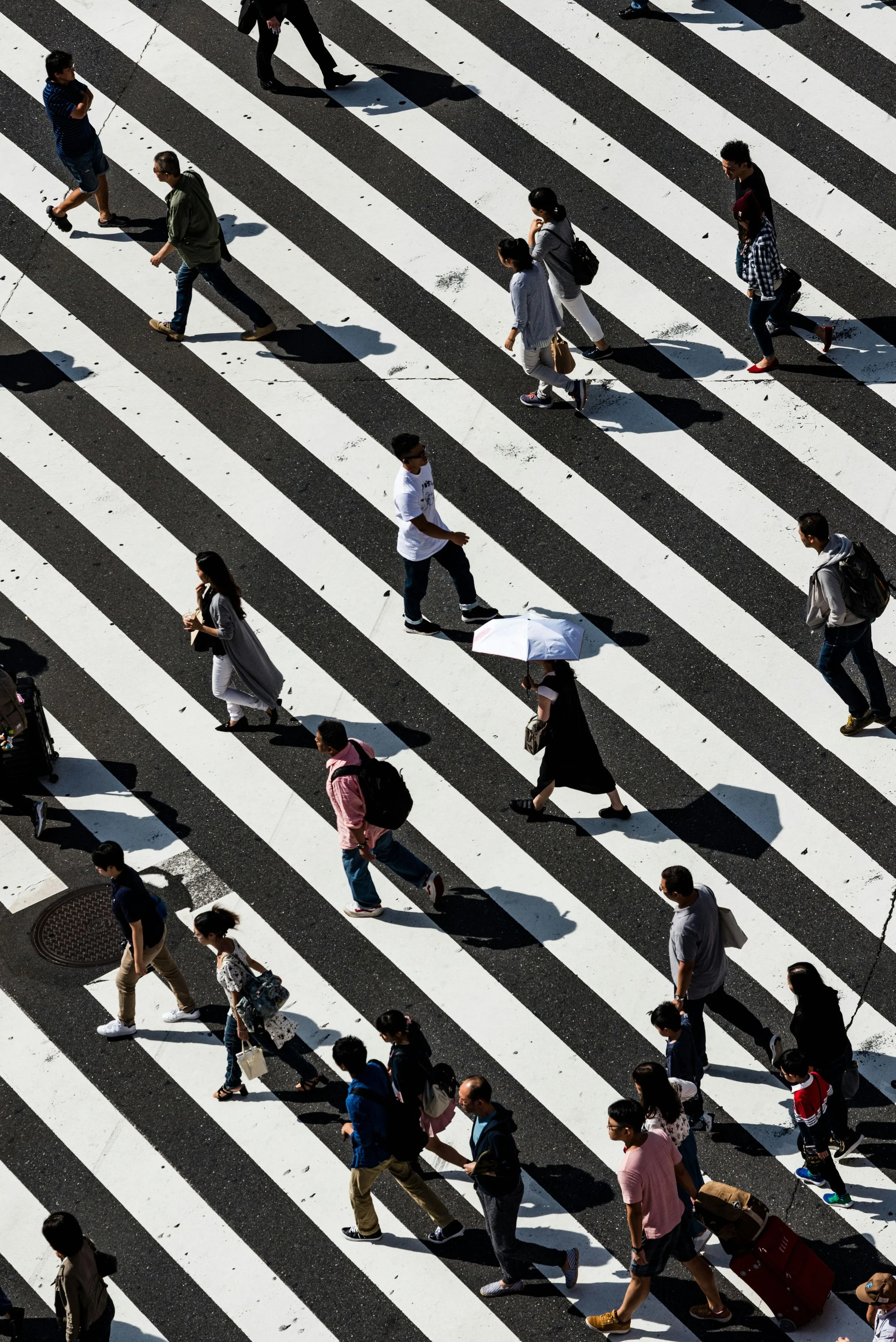 People walking across a pedestrian crosswalk with black and white stripes, seen from above.