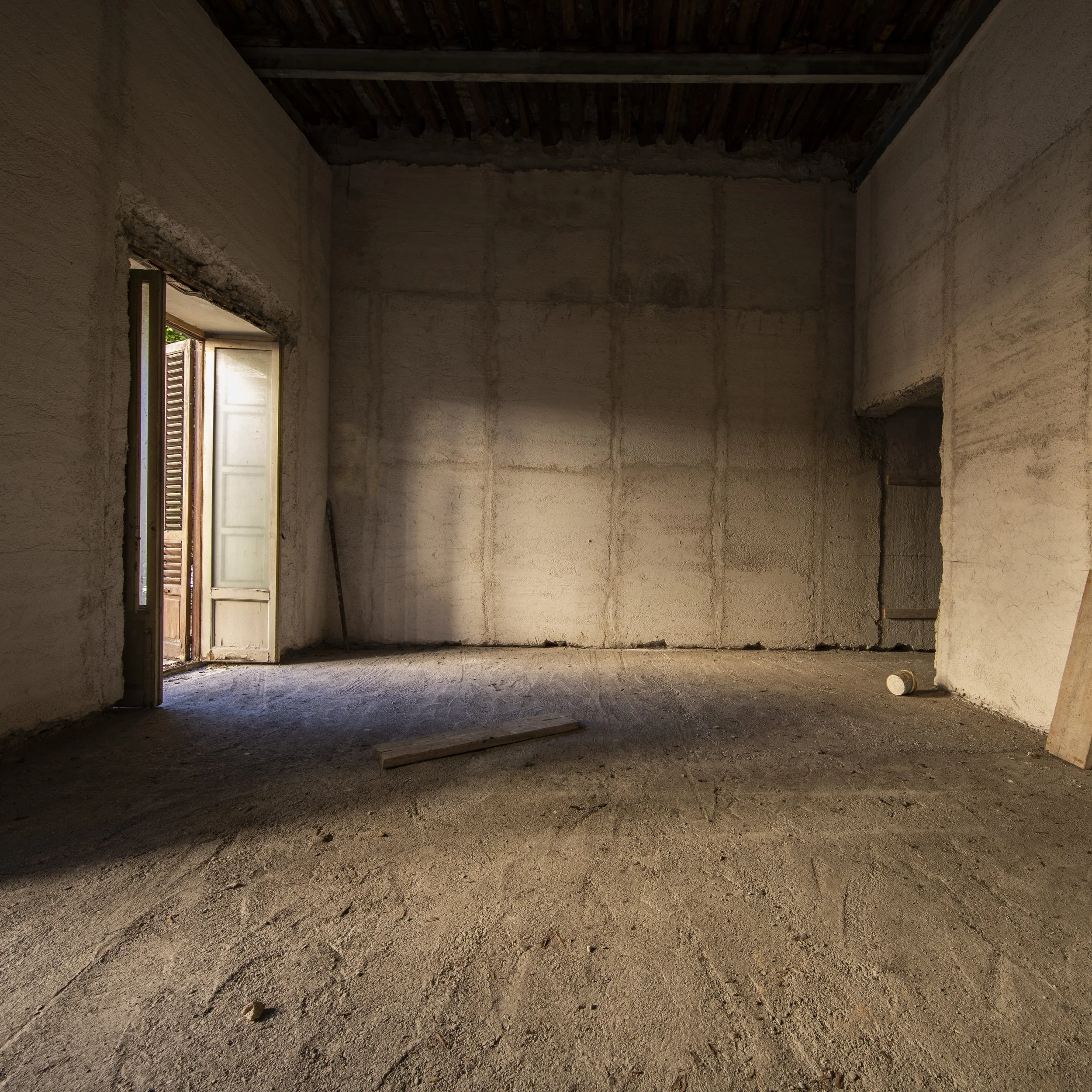 Empty room under construction with unfinished walls, floor, and ceiling, with a partially open door on the left letting in natural light.