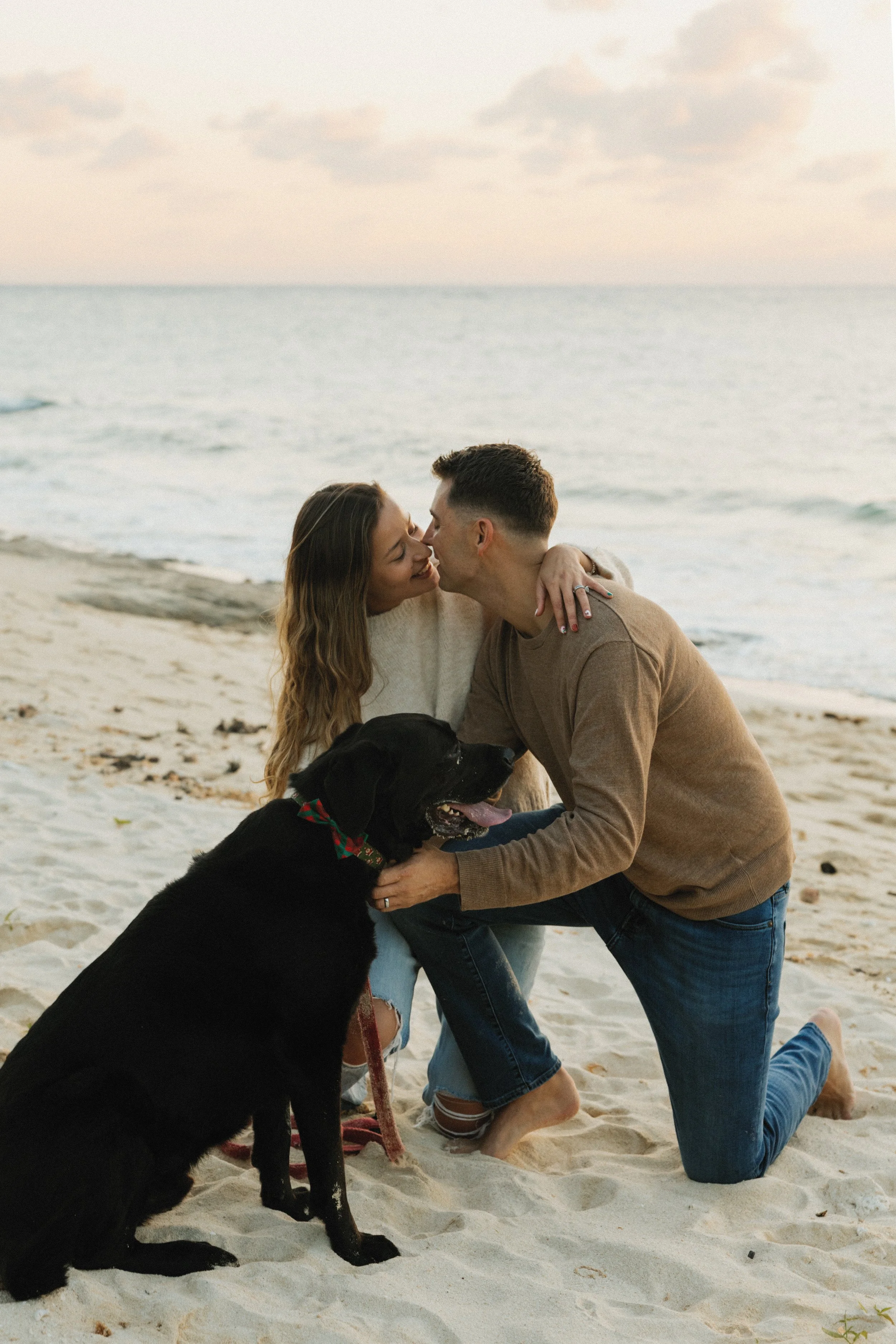 A couple kissing on the beach with their black dog.