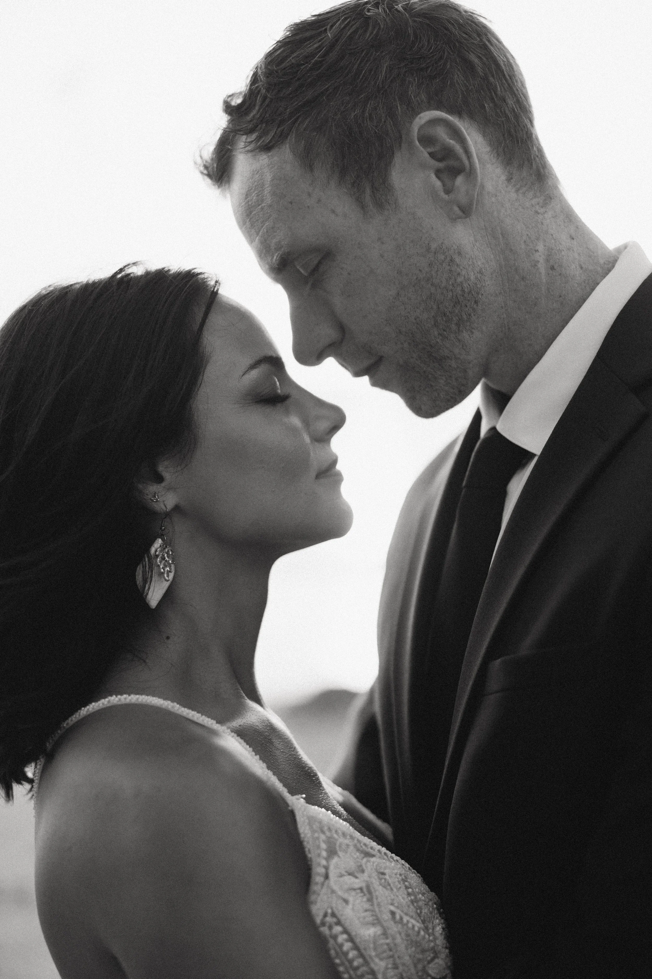 A black-and-white photo of a man and woman close together, with their foreheads touching and eyes closed, showing a moment of intimacy.