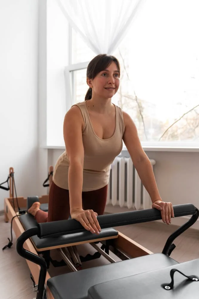 Une femme faisant de l'exercice de poussée sur une machine de rééducation dans une pièce lumineuse avec une fenêtre et des rideaux blancs.