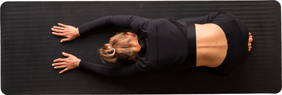 Personne faisant du yoga sur un tapis noir, en position de repose face vers le sol, portant des vêtements de sport noirs.