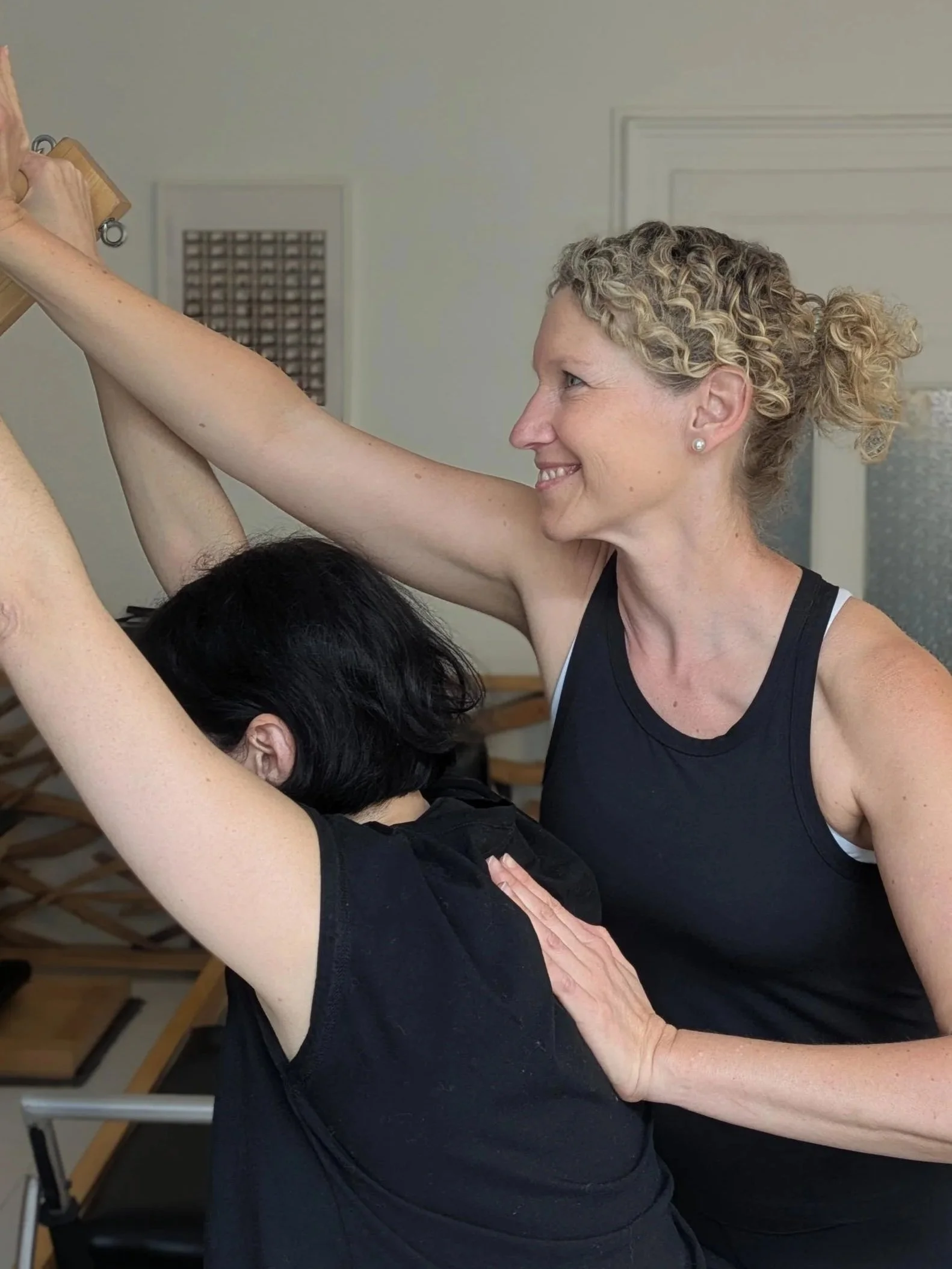 Une femme souriante aide une autre femme à faire de l'exercice de yoga dans une salle intérieure.