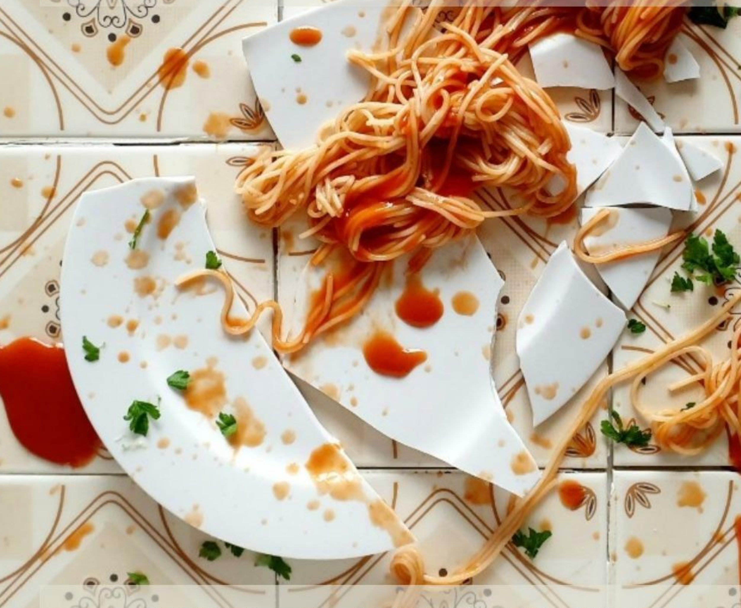 Broken white ceramic plate with spaghetti and sauce, on a decorative tiled surface.