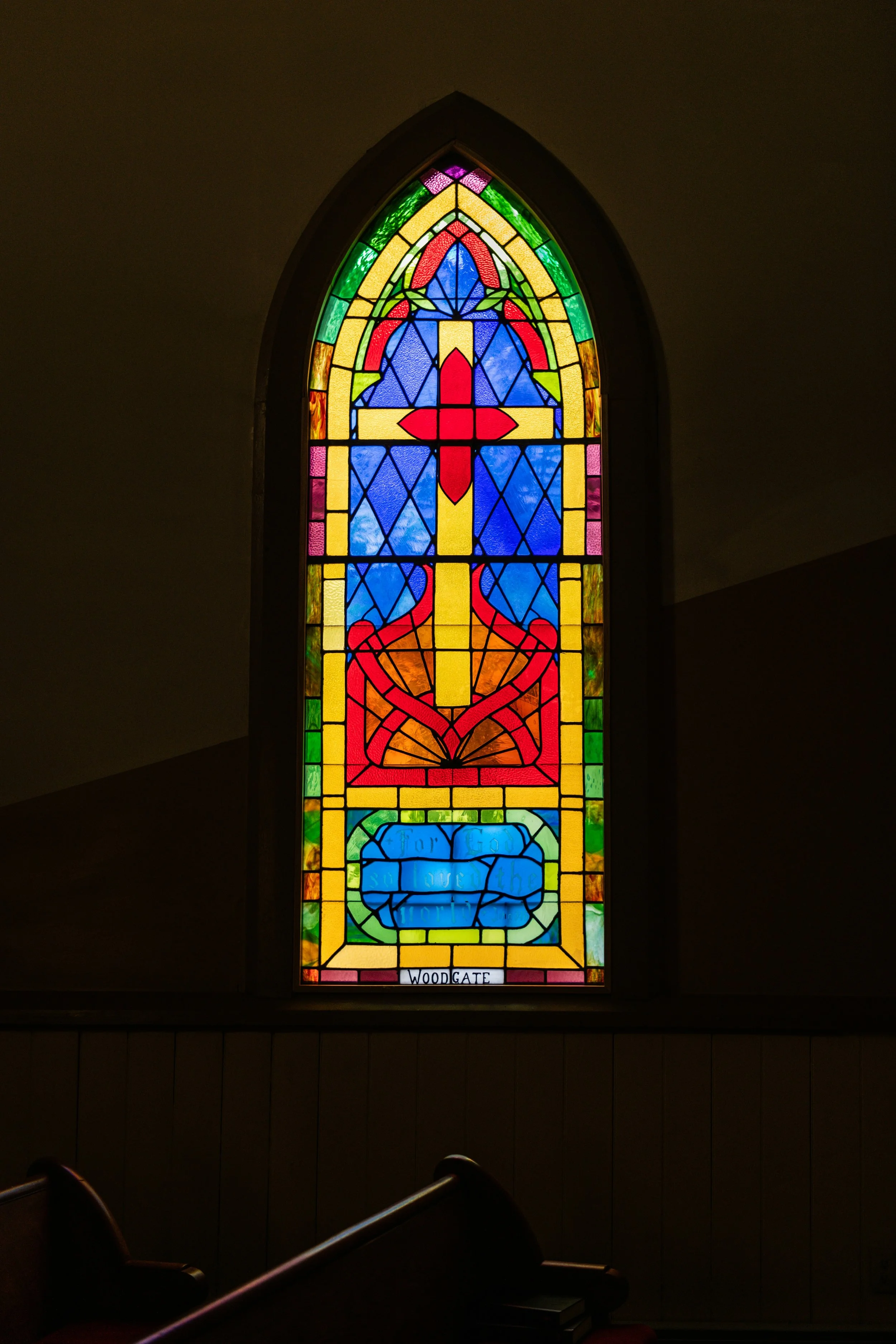 Colorful stained glass window with a cross in the center, surrounded by decorative designs.