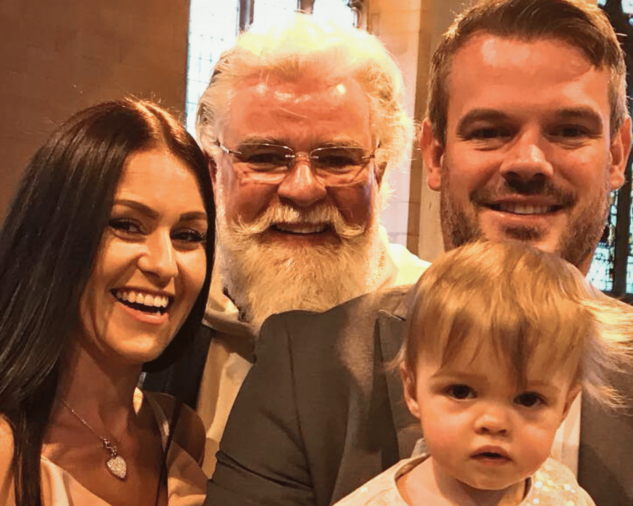 Group of four people smiling and taking a selfie indoors, with a young child in the foreground.