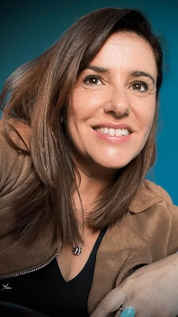 Nathalie Watrin Community manager à Montpellier . Photo de profil , une femme souriante avec des cheveux bruns, portant un manteau marron et un collier, devant un fond bleu.